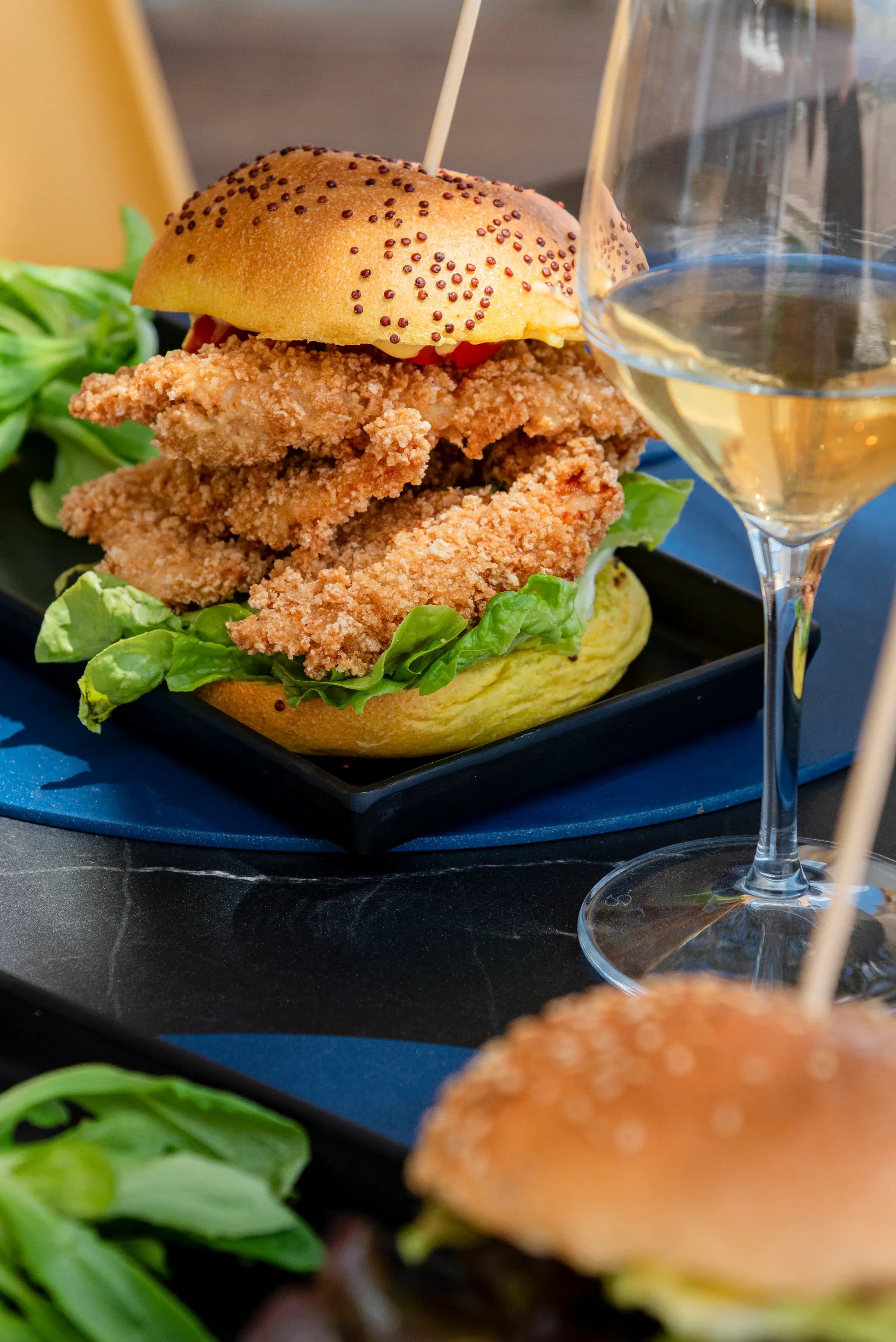 Panino crispy del bistrot su tagliere nero con calice accanto