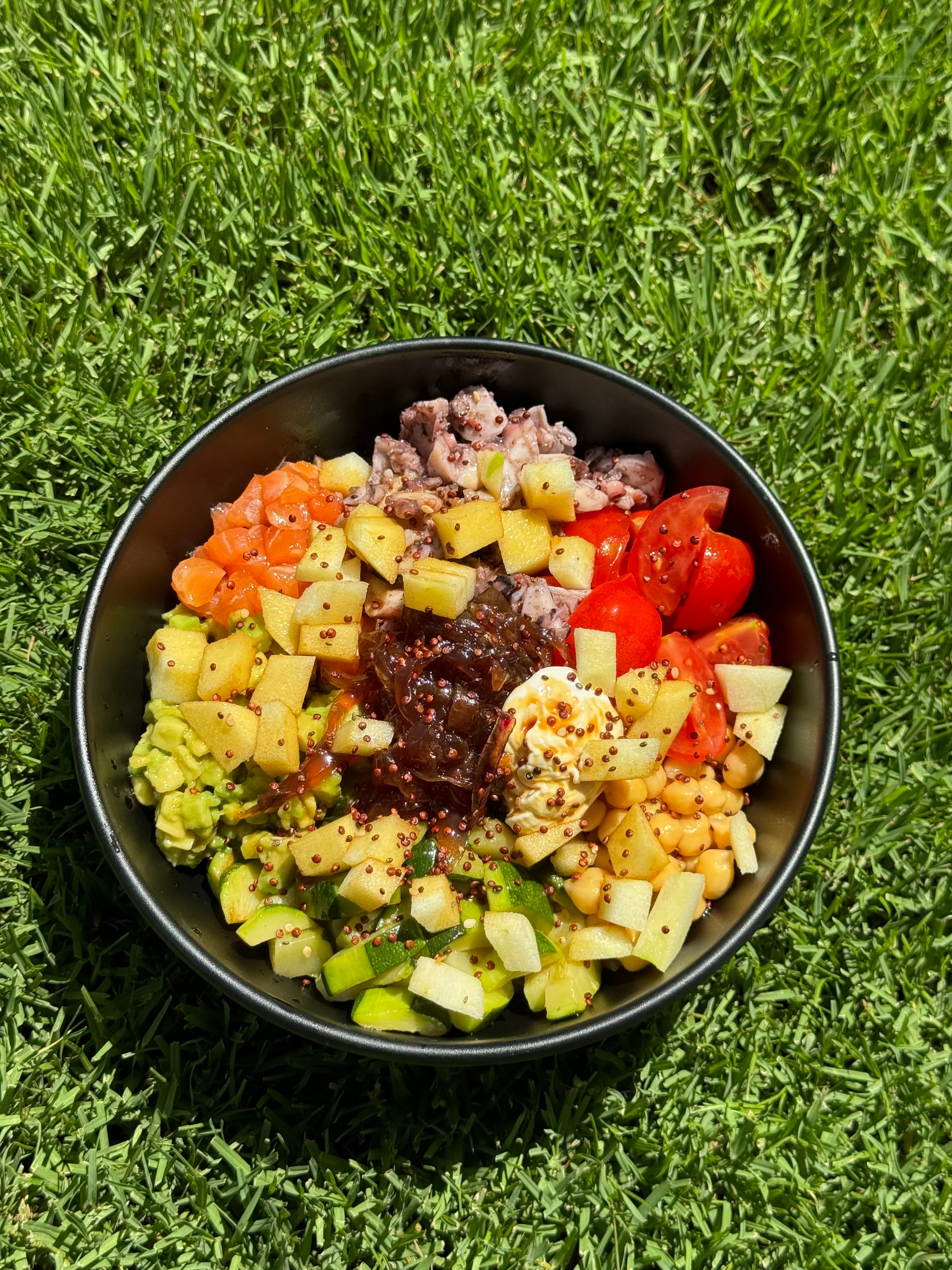 Bowl estiva con pesce, avocado, pomodori e verdure su prato verde